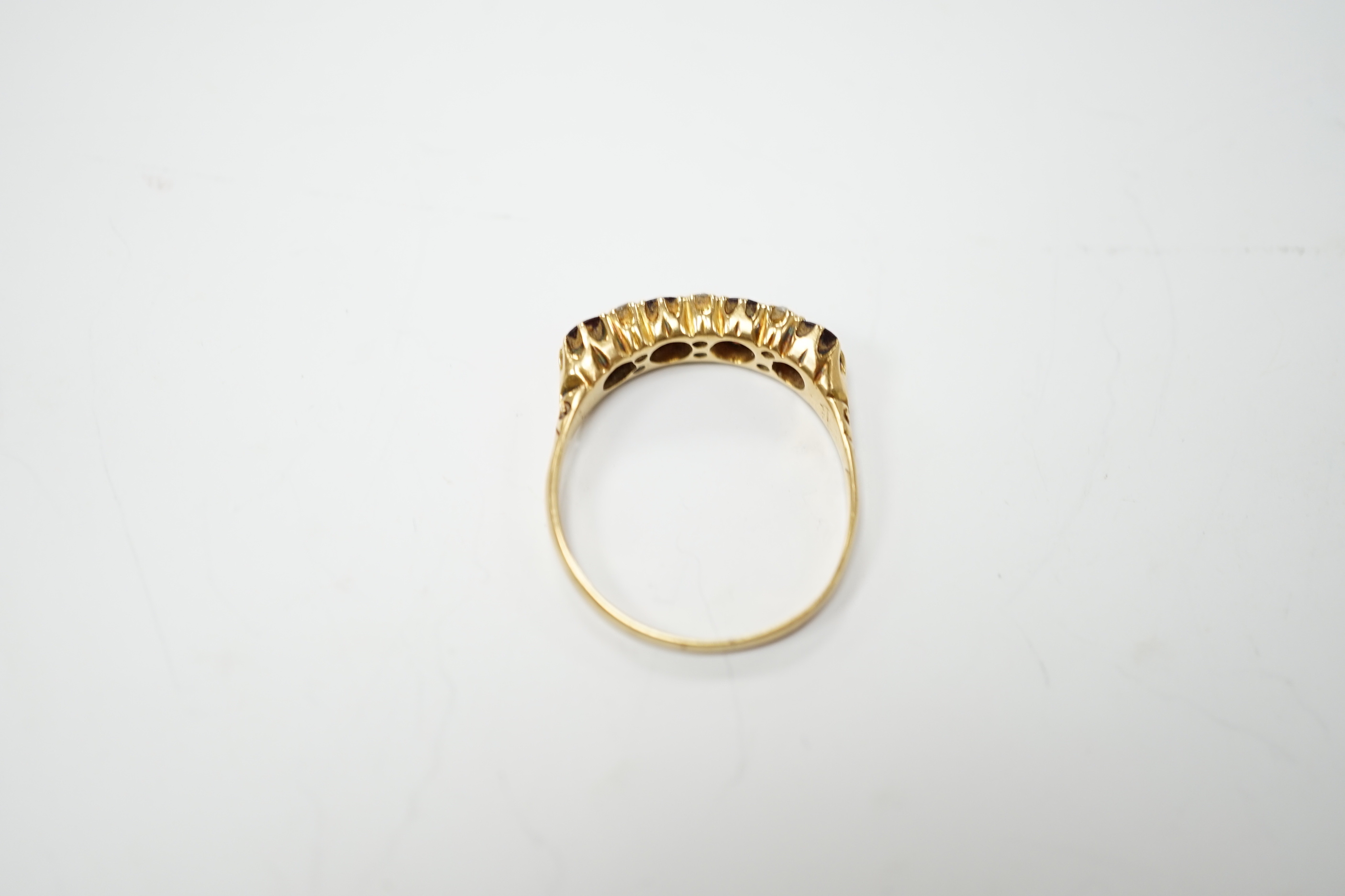 An Edwardian 18ct gold and four stone garnet set half hoop ring, with diamond chip spacers, size R, gross weight 3.6 grams.